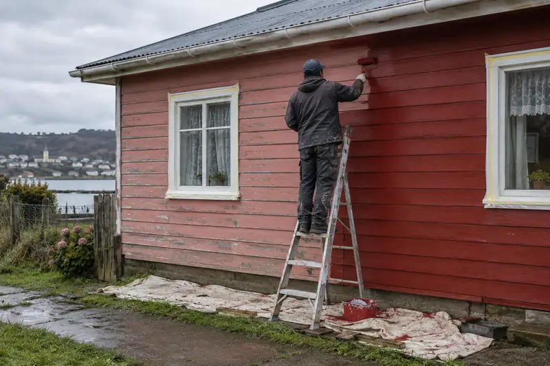 Pintor pintando de rojo el tinglado de una casa de madera